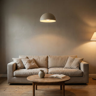 Béžová pohovka s polštáři pod závěsnou lampou, před níž stojí kulatý dřevěný stolek s knihou a vázou.