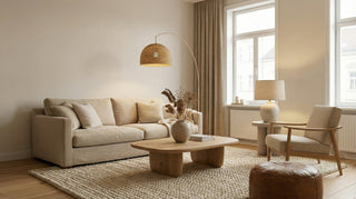 Minimalistický obývací pokoj s béžovou pohovkou, dřevěným konferenčním stolkem, křeslem a stojací lampou u okna.